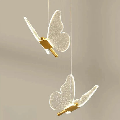 Two butterfly-shaped pendant lights with gold accents on a beige background